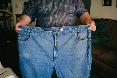 A man shows weight-loss by holding his blue jeans in front of him.