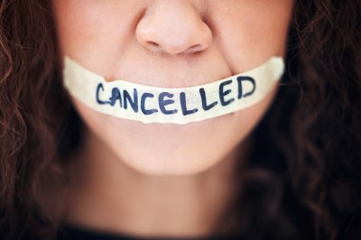 Closeup shot of an unrecognisable woman with tape on her mouth that has the word “cancelled” written on it