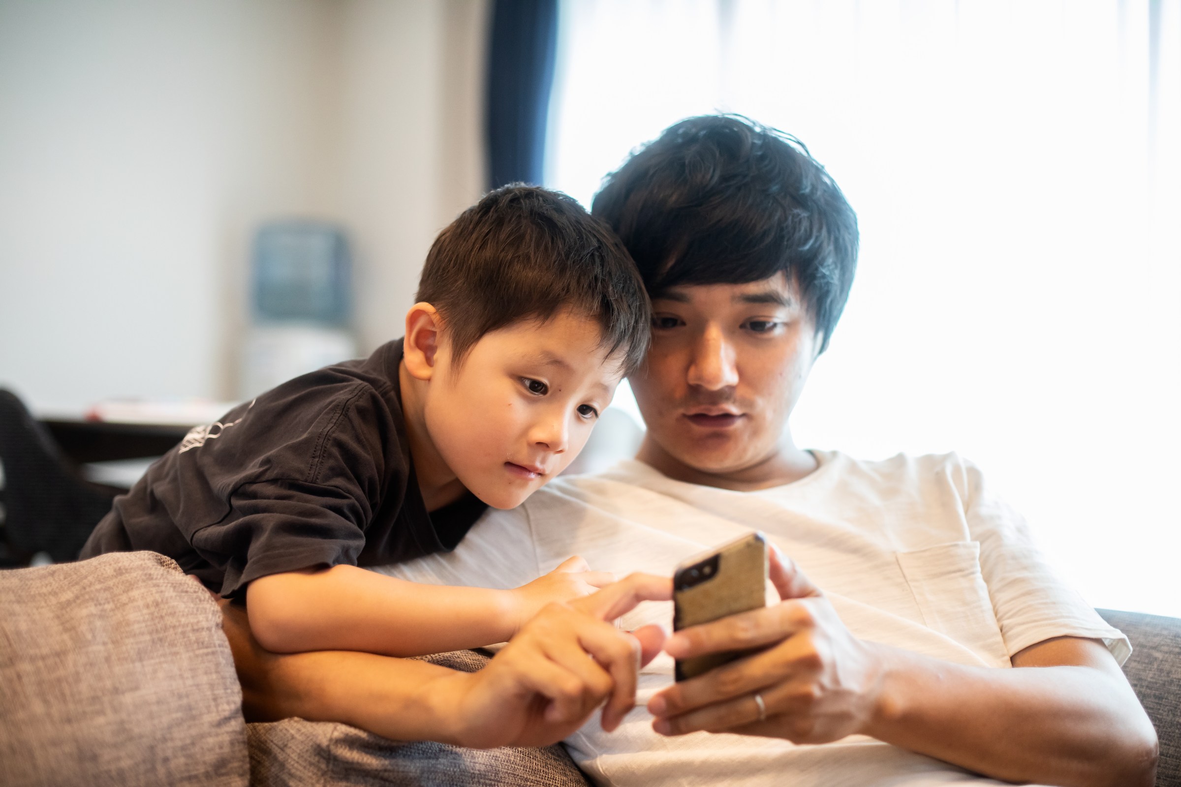 A father and his five-year-old son looking at their smartphones together