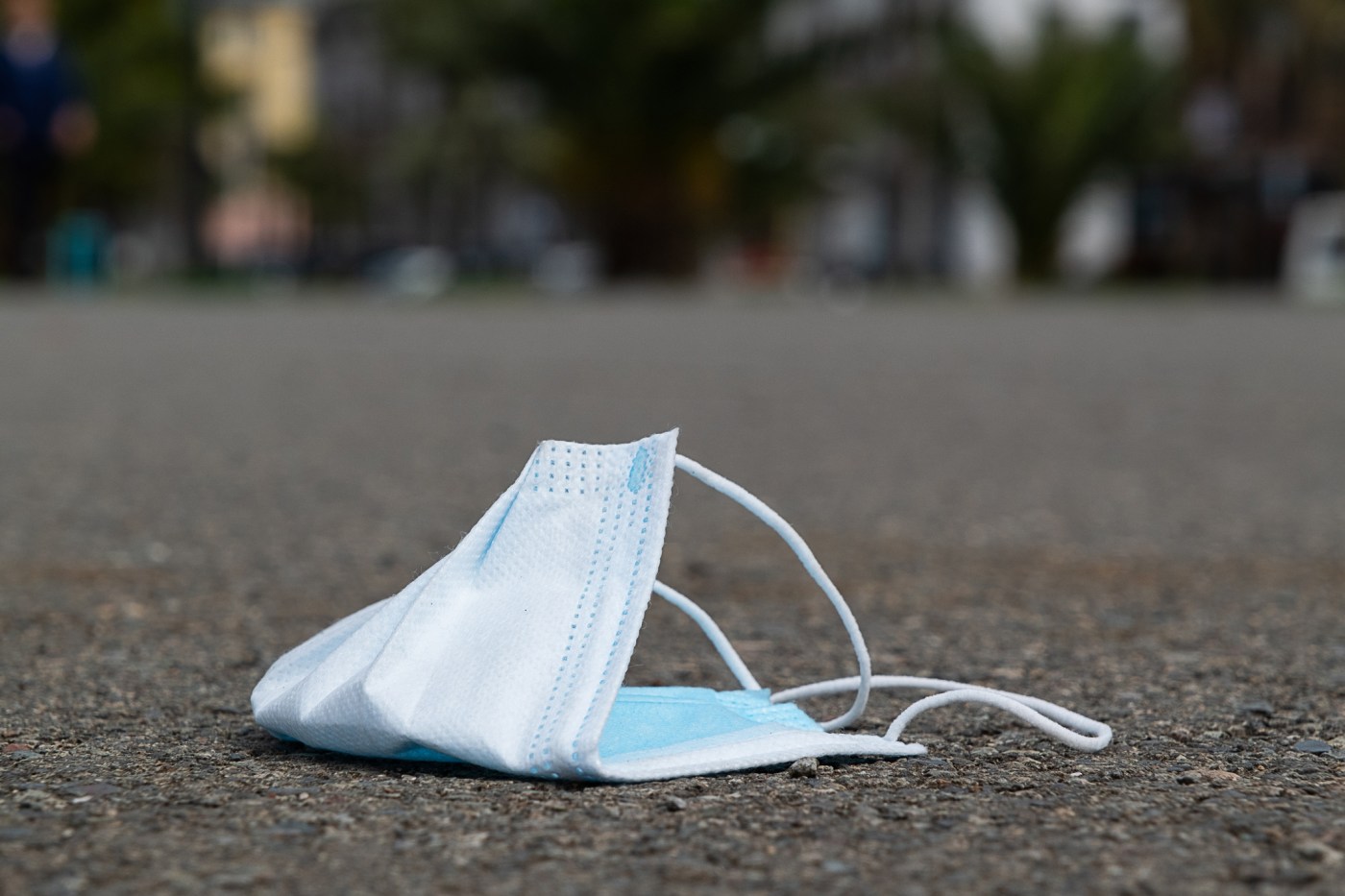 Used lost protective medical face mask on the ground. A disposable mask is lying on the sidewalk outside. Improper disposal of garbage, littering of the planet, a worldwide environmental problem in connection with the coronavirus and the wrong way of life