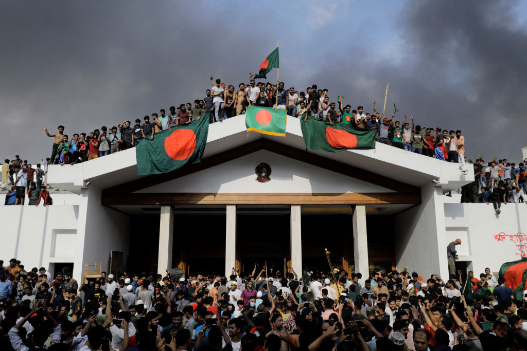 Anti-government protesters display Bangladesh's national flag as they storm Prime Minister Sheikh Hasina's palace in Dhaka on August 5, 2024. (Photo by K M ASAD/AFP via Getty Images)