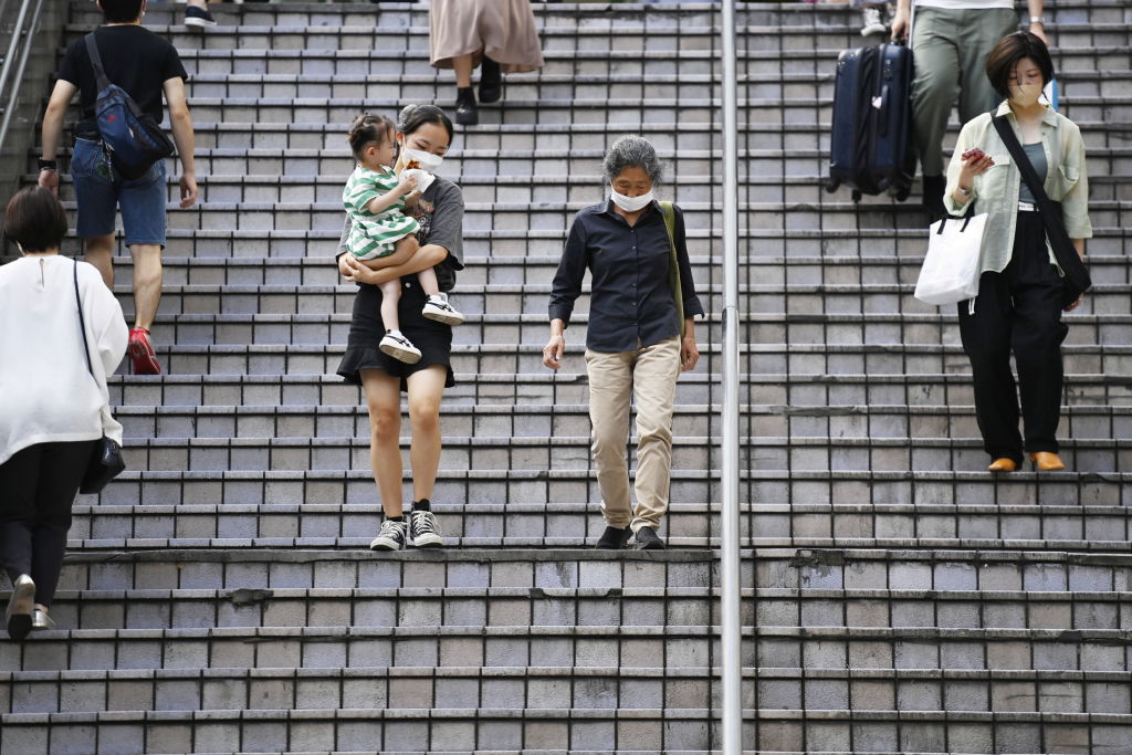 An elderly person moves down a staircase alongside a young woman who carries a child in her arms in Tokyo on October 1, 2022. (Photo by David Mareuil/Anadolu Agency via Getty Images)