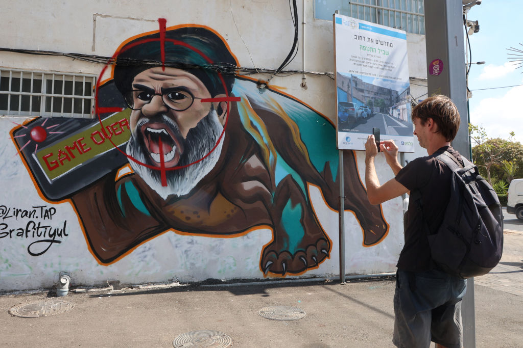 An Israeli takes a picture of graffiti on a street in Tel Aviv depicting the late Hezbollah leader Hassan Nasrallah on September 29, 2024. (Photo by GIL COHEN-MAGEN/AFP via Getty Images)