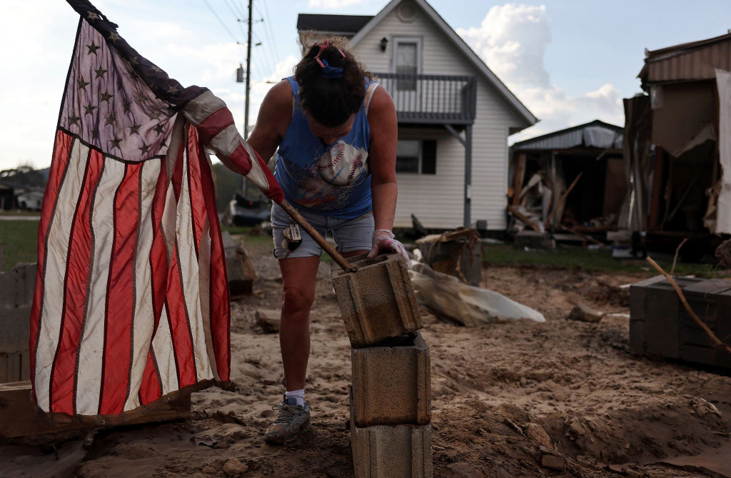 Roxanne Brooks mounts an American flag to a stack of cinderblocks outside her friend's destroyed mobile home in the aftermath of Hurricane Helene flooding on October 6, 2024, in Swannanoa, North Carolina. (Photo by Mario Tama/Getty Images)