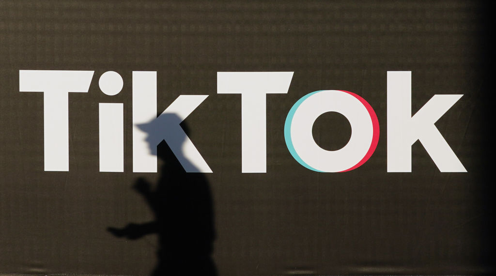 A young man holding a smartphone casts a shadow as he walks past an advertisement for social media company TikTok on September 21, 2020 in Berlin, Germany. (Photo by Sean Gallup/Getty Images)