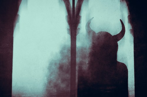 A dark fantasy concept . Of a mysterious devil woman with horns, looking out of a window in an old building, With a blurred, abstract edit.