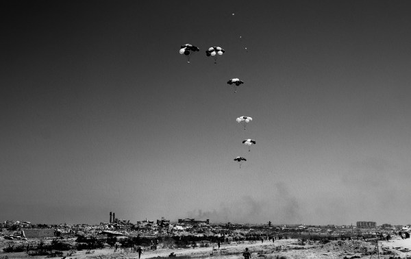 Palestinians rush to the site where parachuted aid packages are landing in the Nuseirat area in the central Gaza Strip during an airdrop above the Israel-besieged Palestinian territory on August 6, 2025. (Photo by EYAD BABA/AFP via Getty Images)