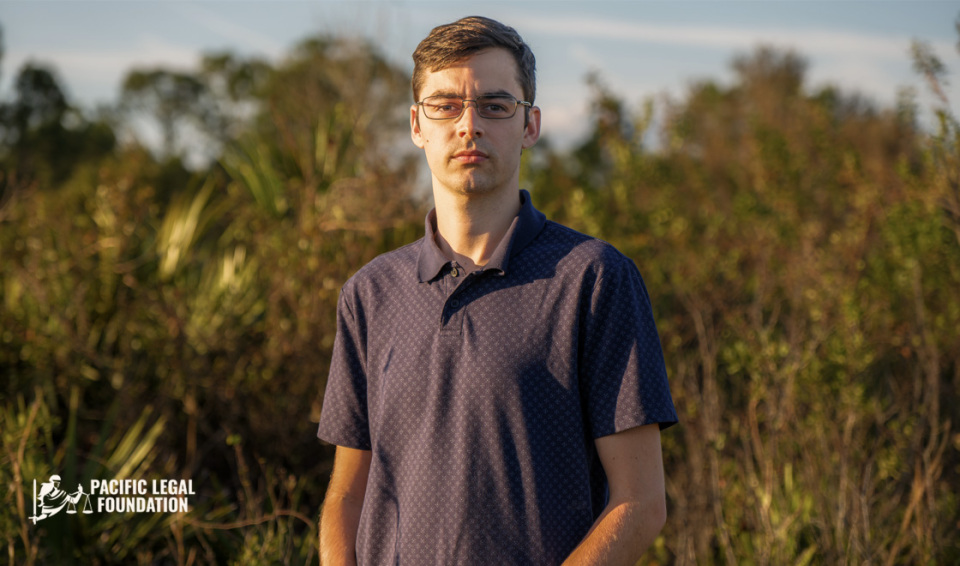 A man standing outside with trees in the background