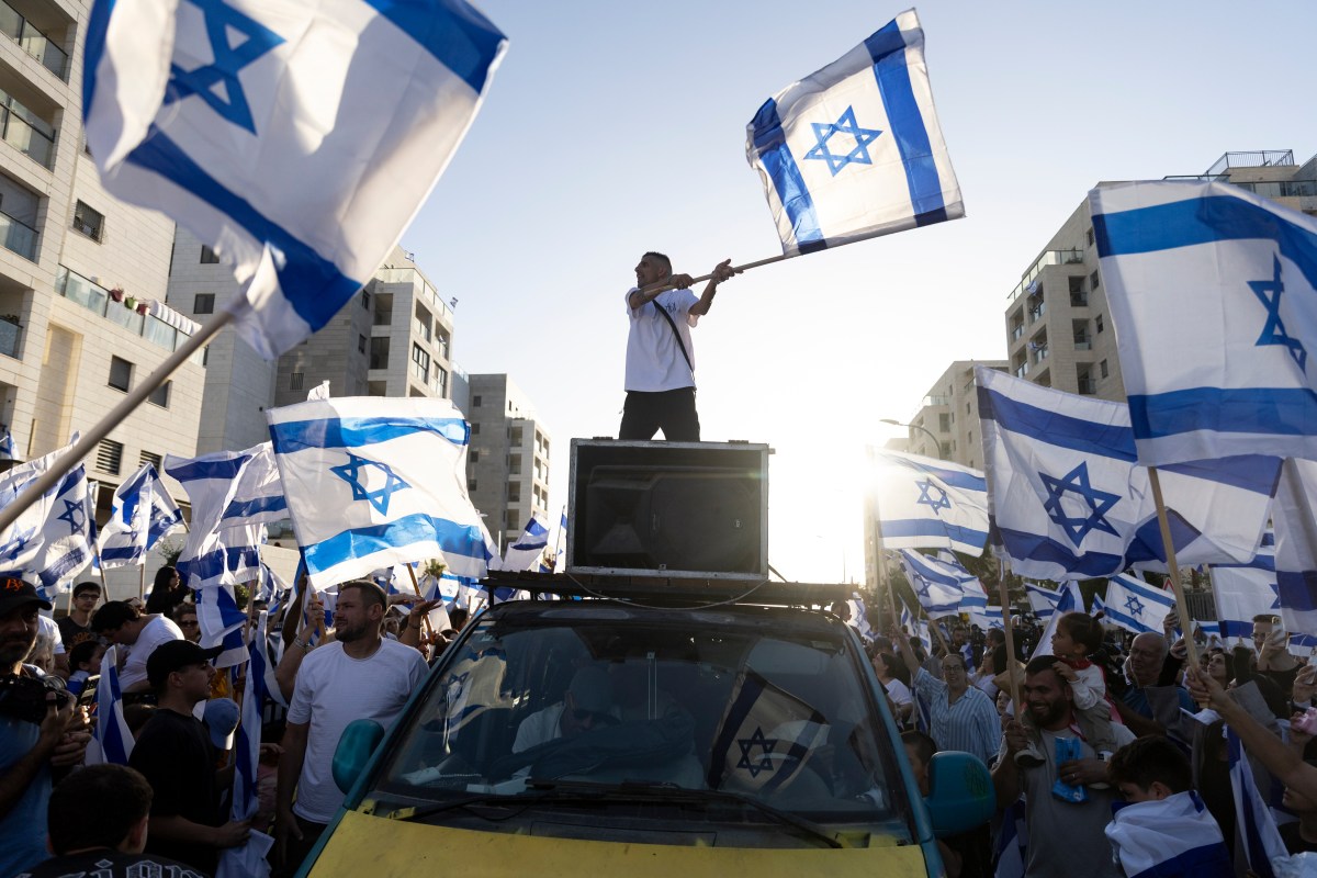 A man standing on top of a car with a flag on top