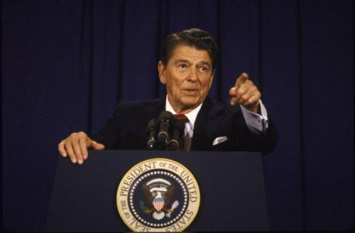 A man in a suit pointing at the camera