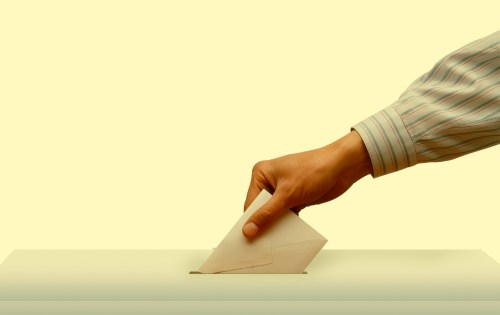 A hand putting a piece of paper into a ballot box