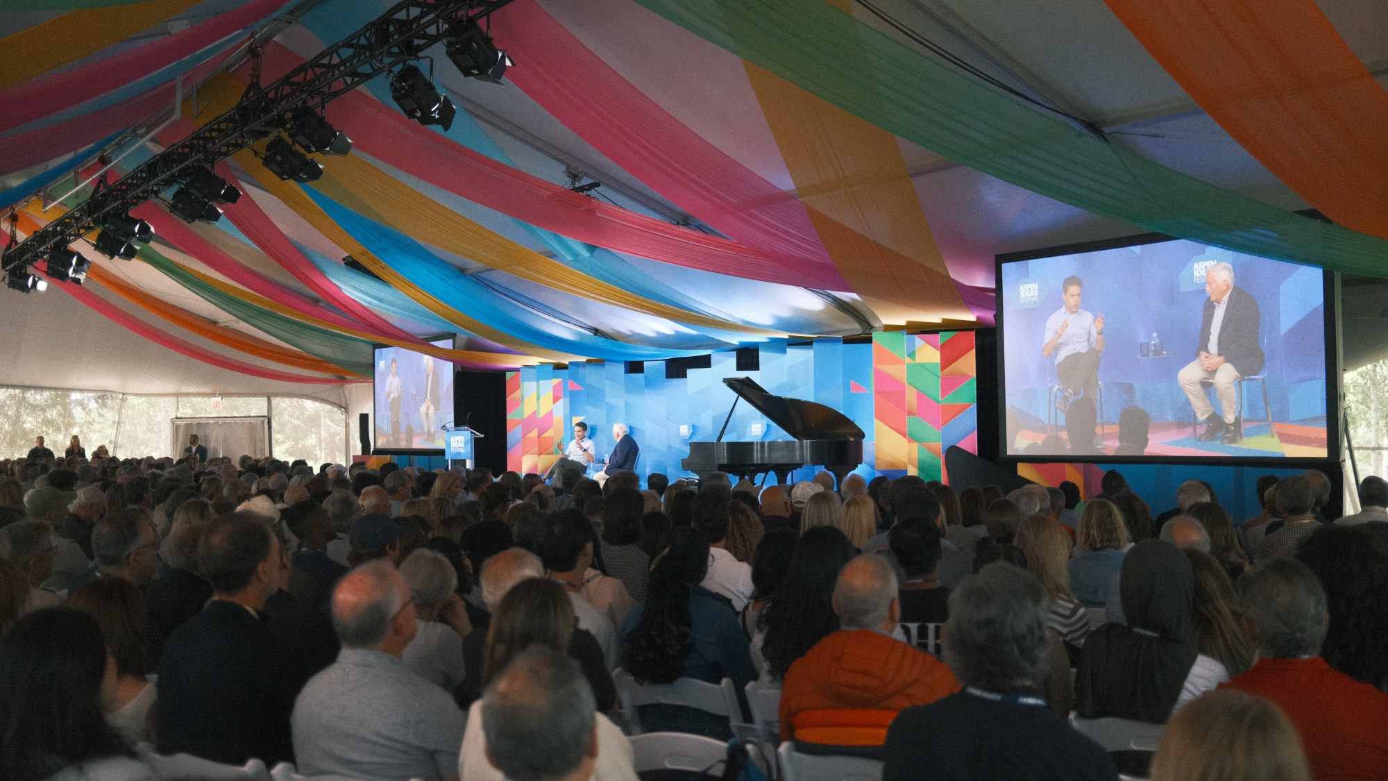 A group of people in a room with a stage and a piano