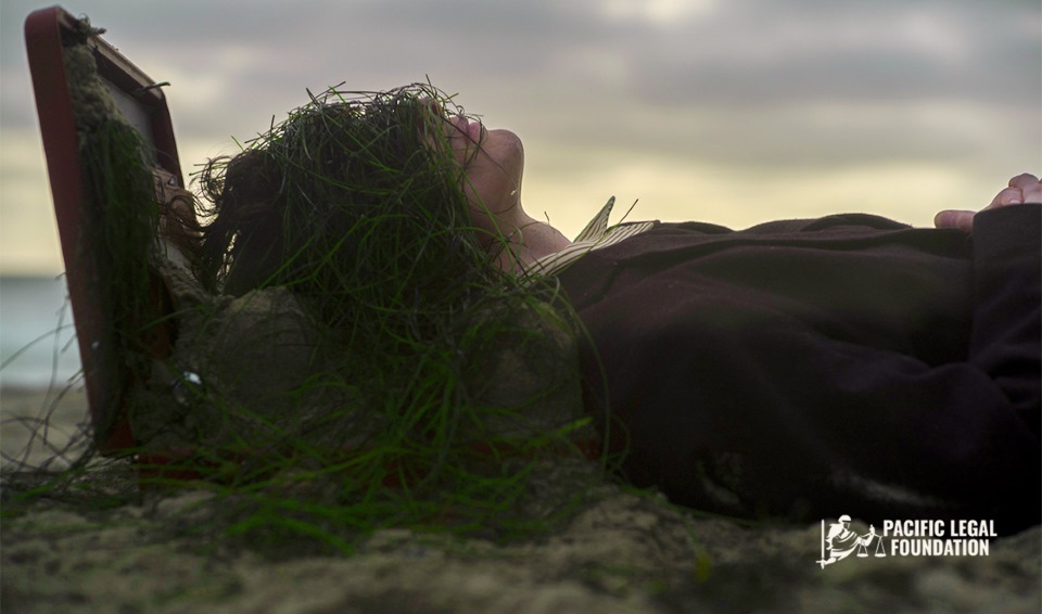 A woman lying in the sand with grass on her head